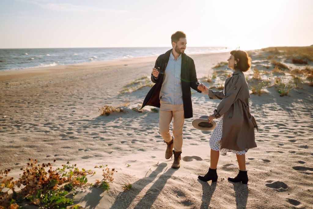 Stylish couple walking and hugging by the sea. Lovely hipster couple enjoying time together.