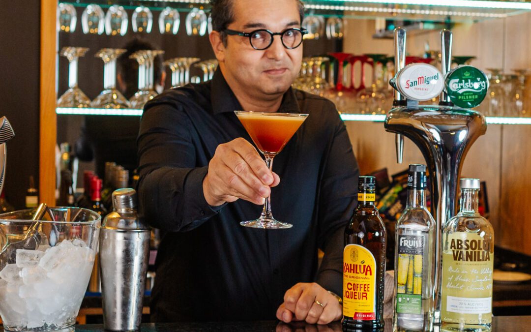 A middle aged man dressed in black holding an espresso martini behind the bar
