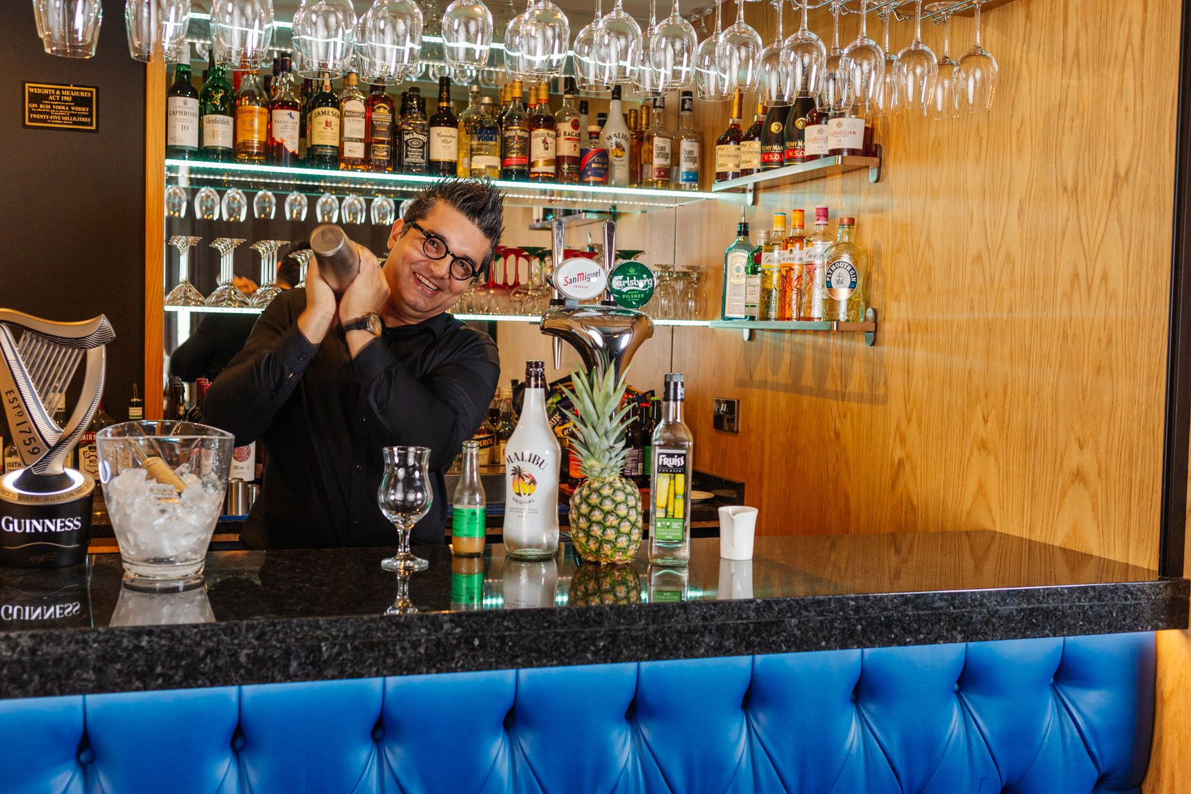 A middle aged man dressed in black shakes a pina colada cocktail shaker behind the bar at The Carlton Hotel in Ilfracombe