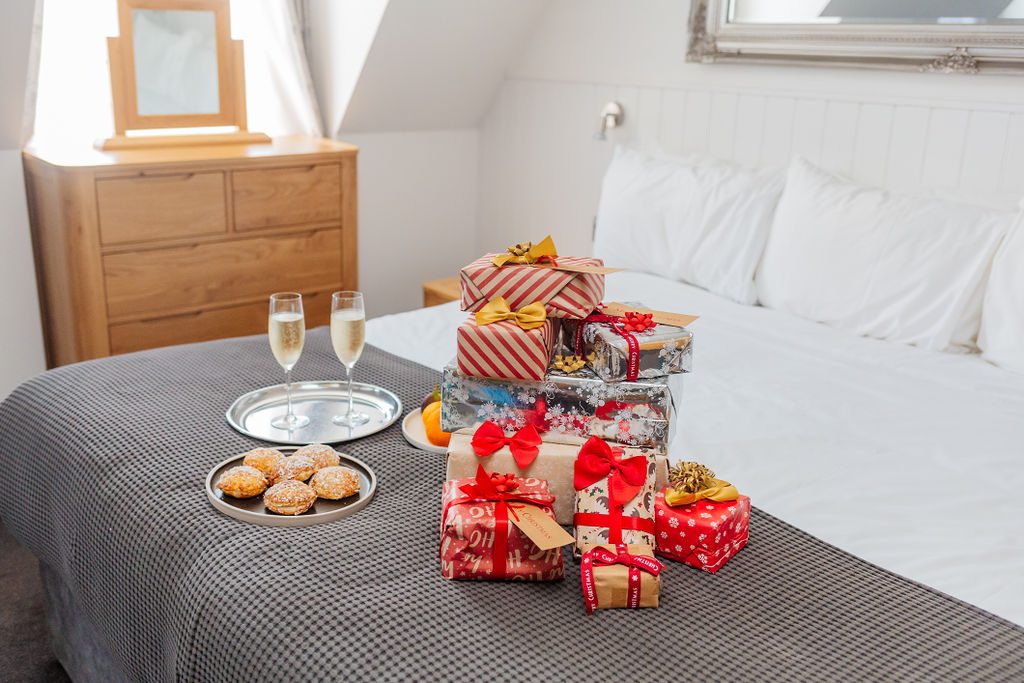 A hotel bed at The Carlton Hotel in Ilfracombe is stacked high with christmas gifts. A plate of mince pies and two glasses of champagne are on a tray on the bed