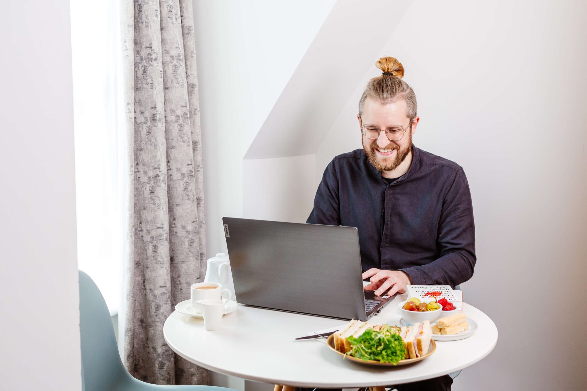 A young white man sat a laptop in a hotel room on a workation in North Devon
