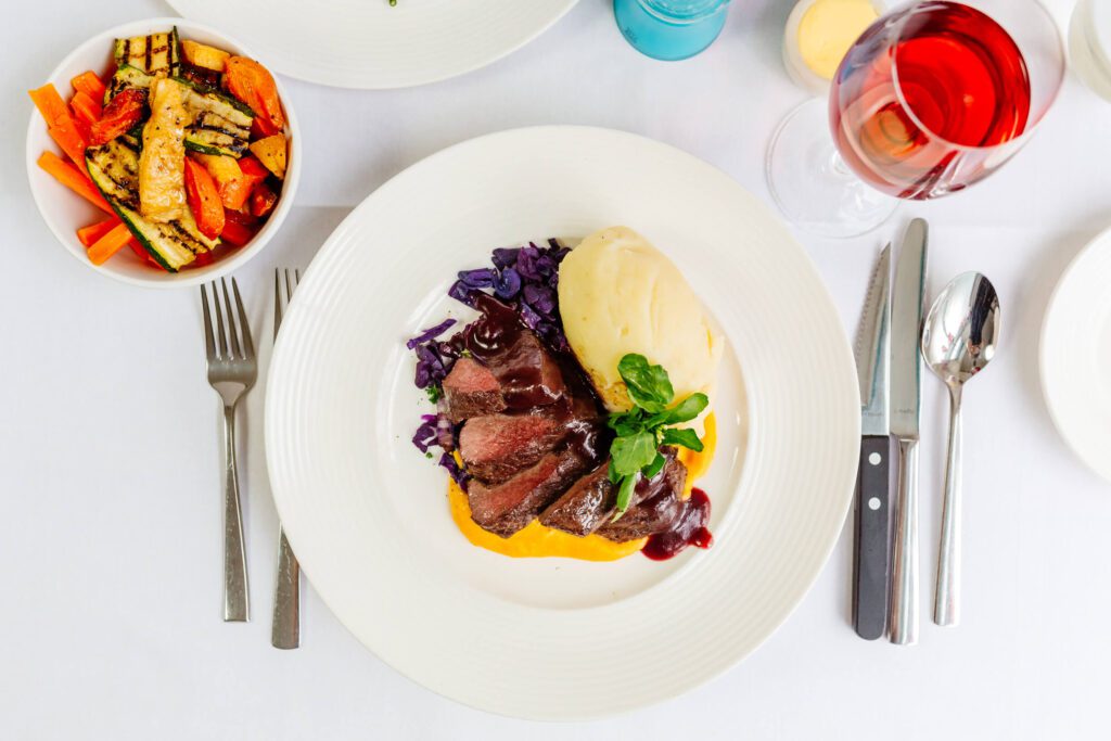 A plate of food on a restaurant table with a glass of wine and a side dish of vegetables