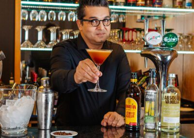 A middle aged man dressed in black holding an espresso martini behind the bar