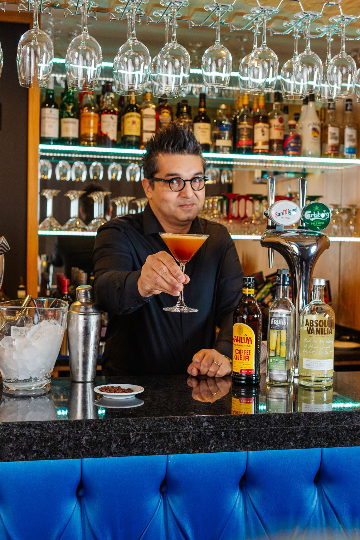 A middle aged man dressed in black holding an espresso martini behind the bar